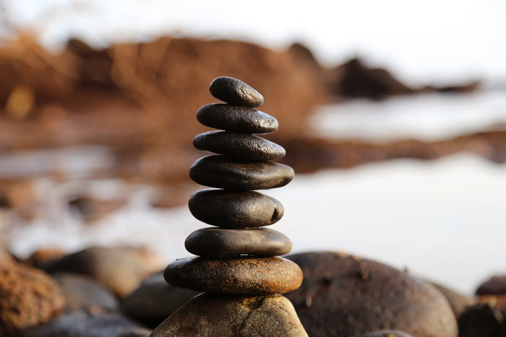 A serene stack of smooth stones, meticulously balanced by the water's edge, reflects the essence of a calm, focused, and balanced mind.